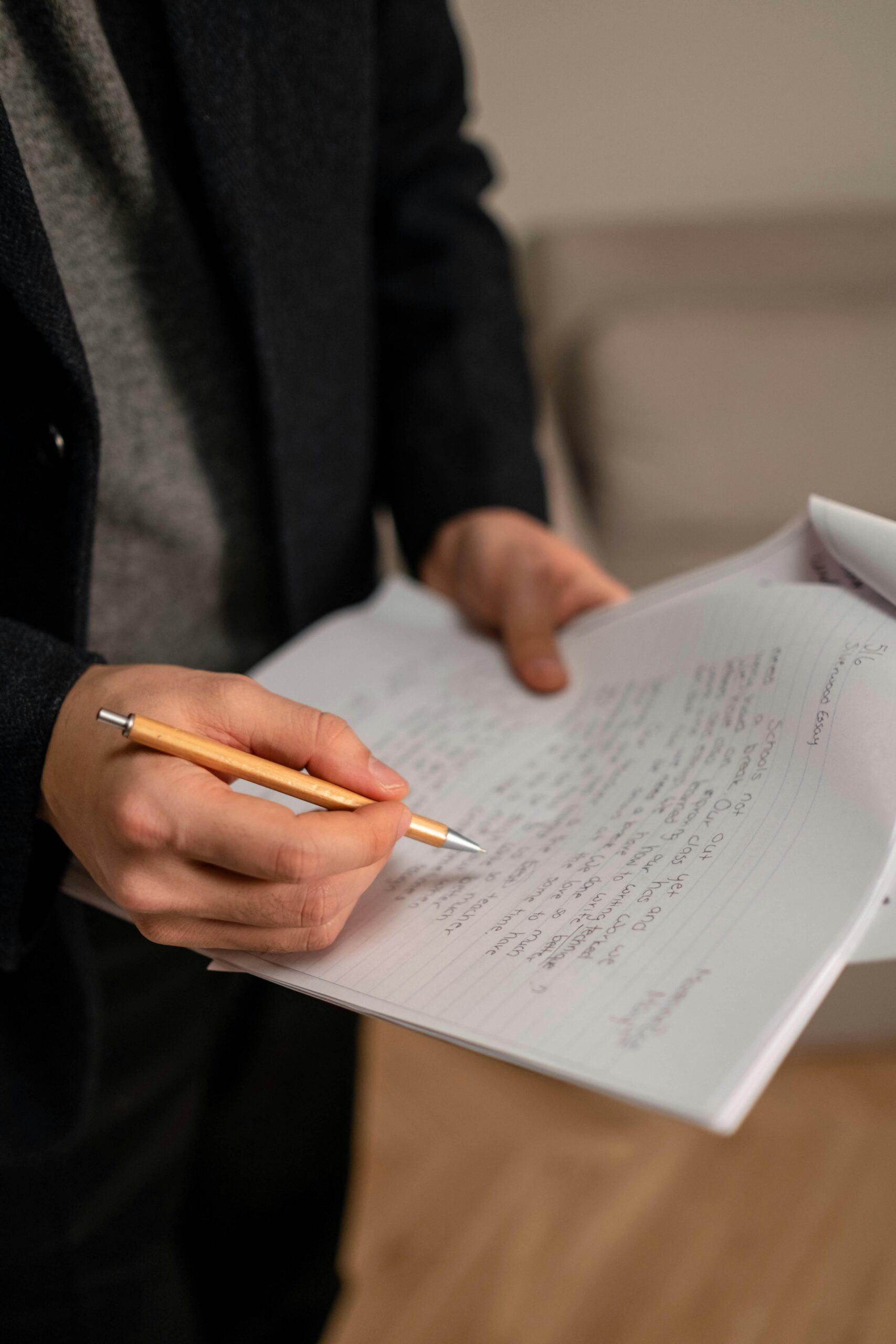 Close-up of a person holding a pen and writing notes on paper indoors.